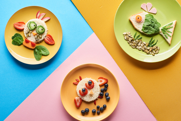 vista superior de platos con animales de lujo hechos de comida sobre fondo azul, amarillo y rosa
 - Foto, Imagen