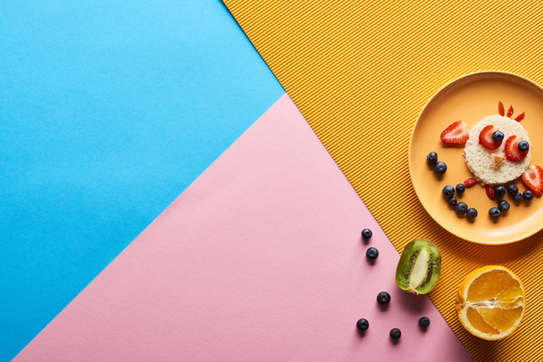 Teller mit ausgefallenen Tieren aus Futter für das Kinderfrühstück auf blauem, gelbem und rosa Hintergrund - Foto, Bild