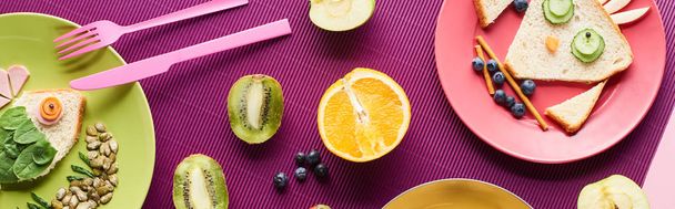 top view of plates with fancy animals made of food near fruits on purple background, panoramic shot - 写真・画像