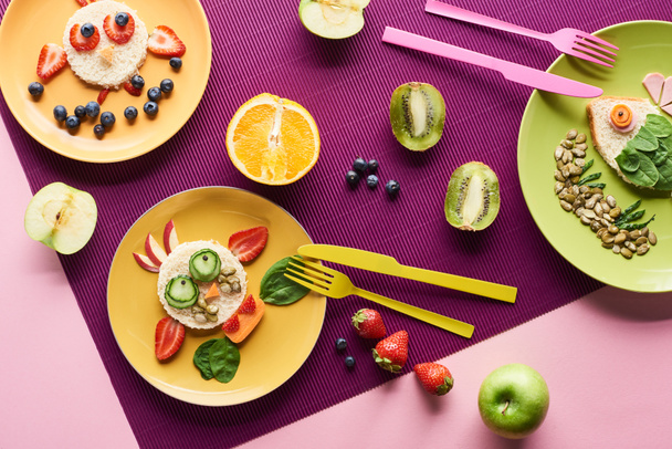 top view of plates with fancy animals made of food near fruits on purple background - Photo, Image