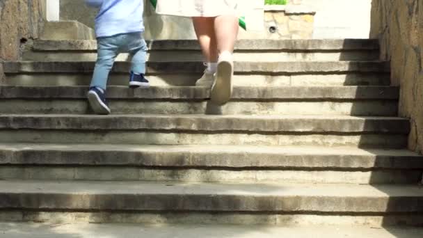 Close up of woman helping her little child boy to climb the stairs by holding his hand. Stock footage. Mother with small kid son walking up the stairs. - Footage, Video
