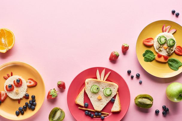 Κορυφαία όψη των πλακών με φανταχτερά ζώα φτιαγμένα από φαγητό σε ροζ φόντο με φρούτα - Φωτογραφία, εικόνα