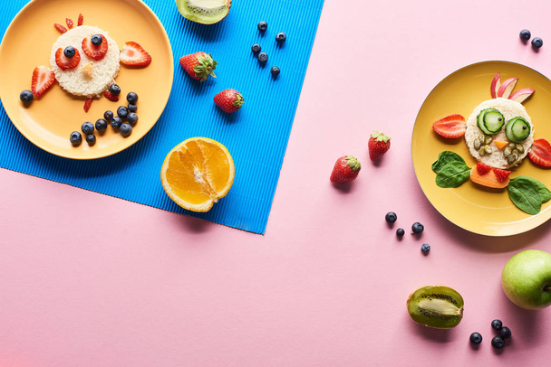top view of plates with fancy animals made of food on blue and pink background with fruits - Photo, Image