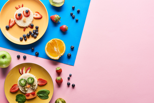 top view of plates with fancy animals made of food on blue and pink background with fruits - Photo, Image
