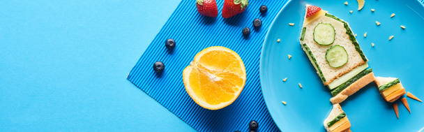 вид сверху на тарелки с фантастической ракетой из продуктов питания на синем фоне с фруктами, панорамный снимок
 - Фото, изображение