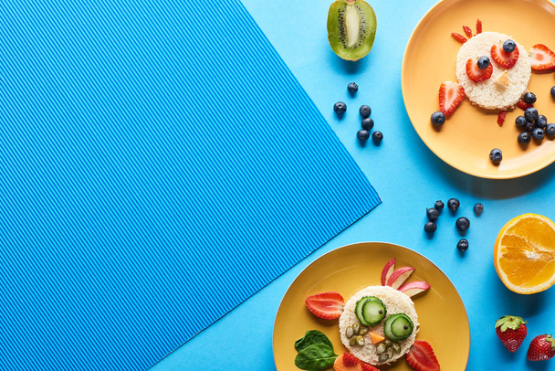 青い背景に食べ物で作られた派手な動物とプレートのトップビュー - 写真・画像