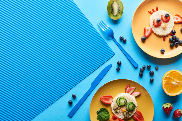вид сверху на тарелки с модными животными, сделанными из пищи на синем фоне
 - Фото, изображение