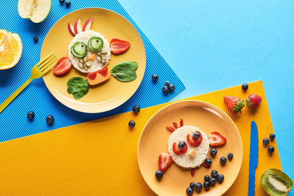 top view of plates with fancy animals made of food on blue and yellow background - Photo, Image