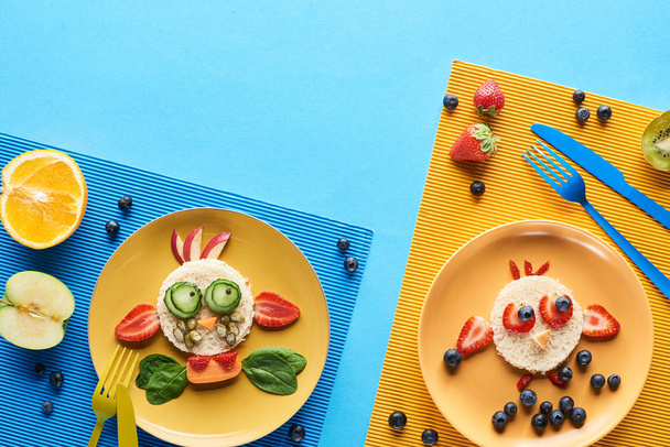 top view of plates with fancy animals made of food on blue and yellow background - Fotó, kép