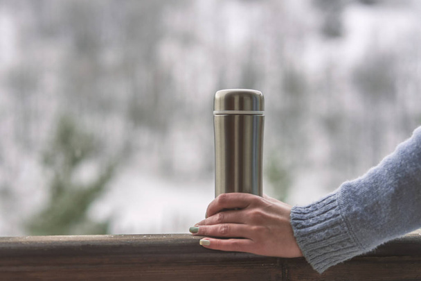 A girl holding a thermos with a hot drink. A mug of coffee in he - Foto, Imagem