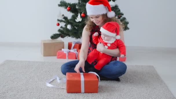 Gezinsvakantie en kerst concept. Jonge moeder met een kind uitpakken van een kerstcadeau - Video