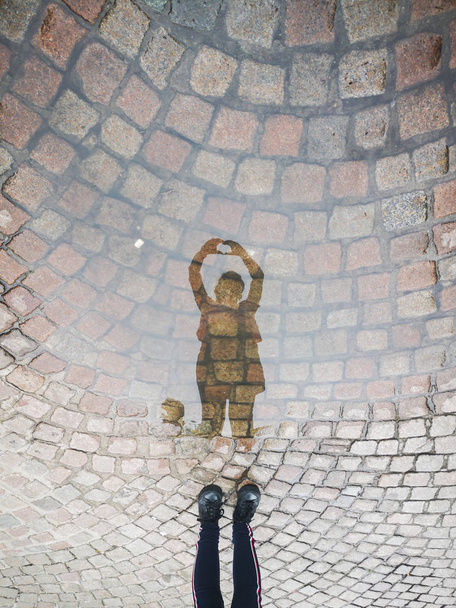 reflet dans une flaque d'eau dans la rue d'une fille formant la figure du cœur avec ses mains
 - Photo, image