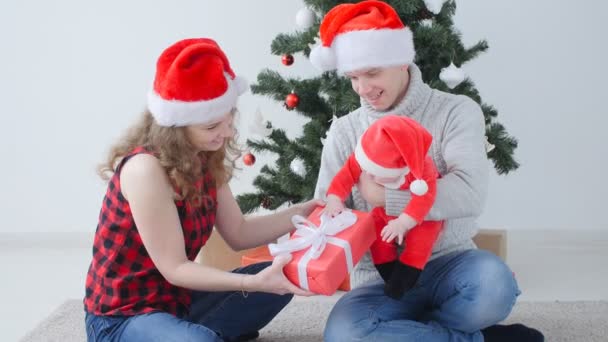 Gezinsvakantie en kerst concept. Jonge moeder en vader met een kind uitpakken een kerstcadeau - Video