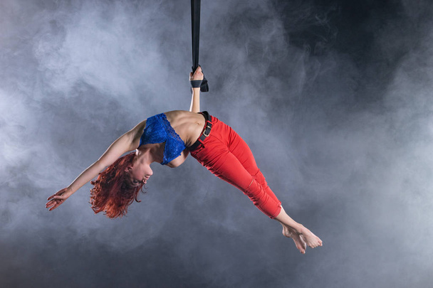 Female athletic, sexy and flexible aerial circus artist with redhead on aerial straps on black background - Valokuva, kuva