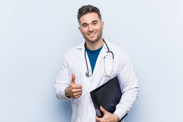 Kaukaski lekarz mężczyzna trzyma folder uśmiechnięty i podnoszenie kciuka w górę - Zdjęcie, obraz