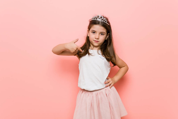 Μικρό κορίτσι φορώντας μια πριγκίπισσα βλέμμα πρόσωπο που σημαδεύει με το χέρι σε ένα χώρο αντίγραφο πουκάμισο, υπερήφανος και σίγουροι - Φωτογραφία, εικόνα