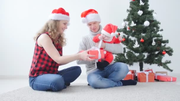 Rodzinne wakacje i koncepcja Bożego Narodzenia. Młoda matka i ojciec z dzieckiem rozpakować prezent świąteczny - Materiał filmowy, wideo
