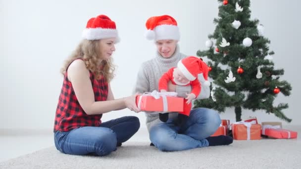 Családi üdülés és karácsonyi koncepció. Fiatal anya és apa egy gyermekkel kicsomagolja a karácsonyi ajándékot - Felvétel, videó