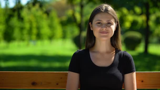 Happy young woman sitting on bench in park and smiling, leisure activity outdoor - Materiaali, video