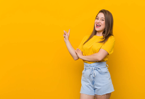 Jovem adolescente vestindo uma camisa amarela sorrindo alegremente apontando com o dedo indicador de distância
. - Foto, Imagem