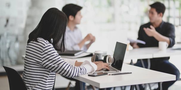 Jovem empresária trabalhadora trabalhando em seu computador portátil com seus colegas de trabalho do sexo masculino
 - Foto, Imagem