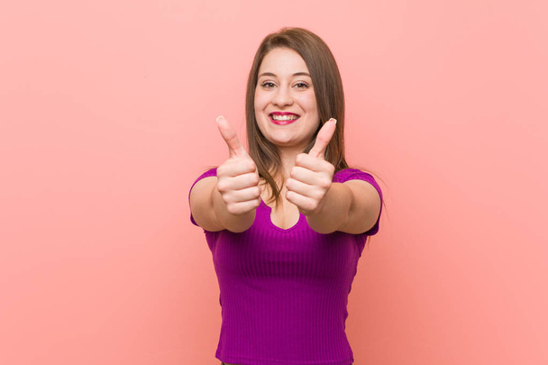 Young hispanic woman against a pink wall with thumbs ups, cheers about something, support and respect concept. - Photo, Image