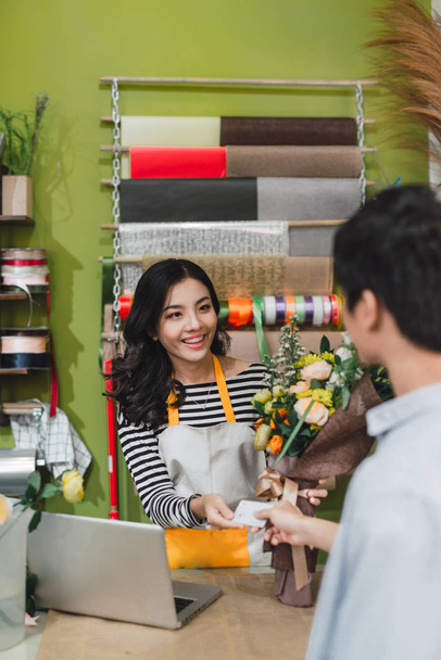 люди, шоппинг, продажа, флористика и потребительство концепция - счастливый улыбающийся флорист женщина делает букет для и мужчина или клиент в цветочном магазине
 - Фото, изображение