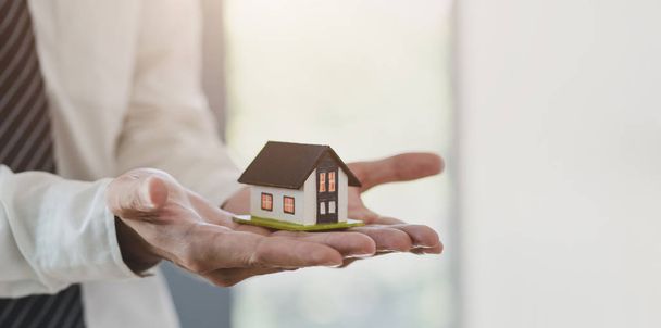 Koncepcja ubezpieczenia nieruchomości: Agent ubezpieczeniowy posiadający model domu w ręku - Zdjęcie, obraz