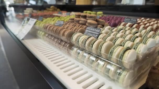 Assortment of colorful traditional French macarons laying in rows on market counter, food concept. Action. Colorful cakes on the counter of the store, sweet meringue-based confection, close up. - Footage, Video