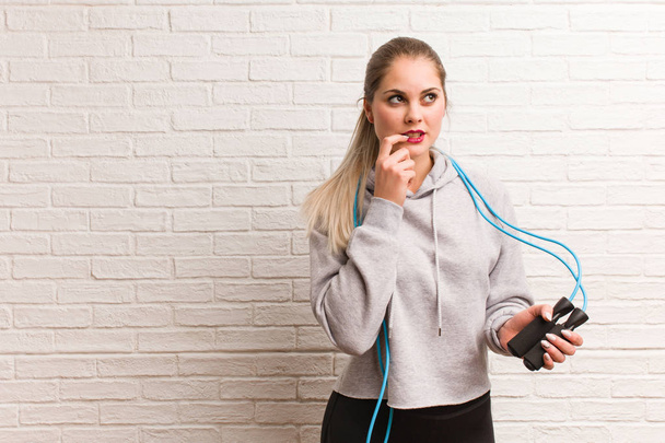 Young fitness russian woman holding a jump rope against a bricks - Photo, Image