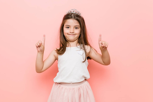La bambina che indossa un look da principessa indica con entrambe le dita anteriori in alto mostrando uno spazio vuoto
. - Foto, immagini