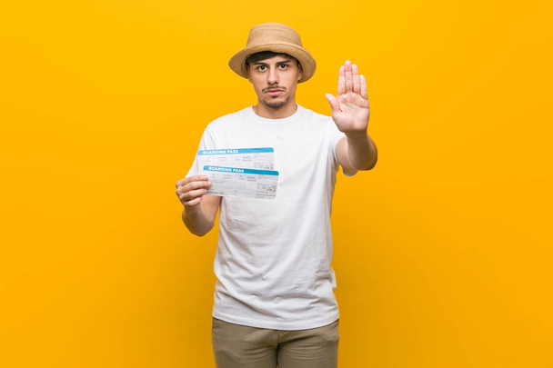 Young hispanic man holding an air tickets standing with outstretched hand showing stop sign, preventing you. - Photo, Image