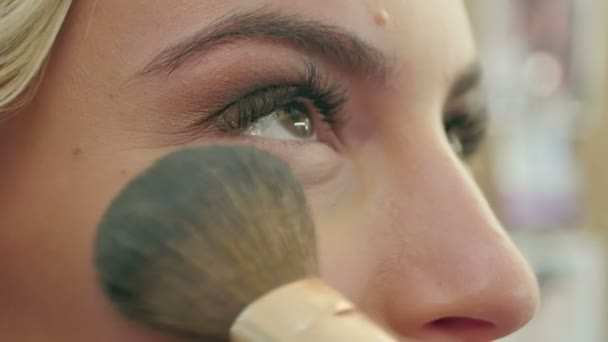 Applying blush makeup with brush to cheekbones of young woman - Video, Çekim