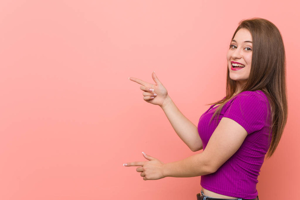 Young hispanic woman against a pink wall excited pointing with forefingers away. - Photo, Image