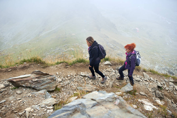 Two women with backpacks hiking on a mountain trail - Zdjęcie, obraz