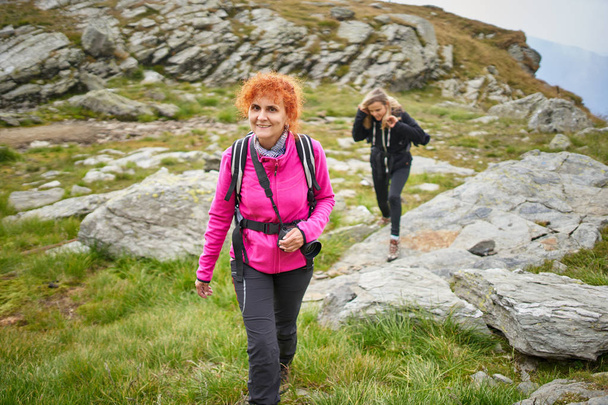 Two women with backpacks hiking on a mountain trail - Φωτογραφία, εικόνα