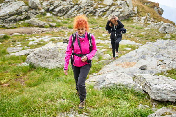 Two women with backpacks hiking on a mountain trail - Фото, зображення