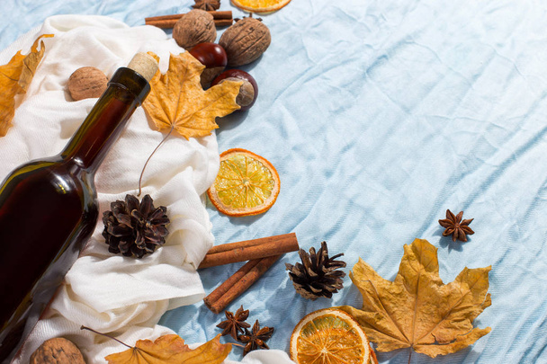A bottle of mulled wine with spices, scarf, dry leaves and oranges on a table. Autumn mood, a method to keep warm in the cold, copy space. - Fotoğraf, Görsel