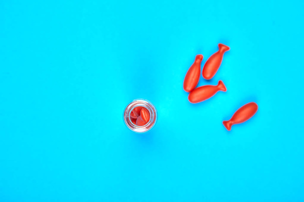 Minimalizm w stylu Omega 3 kapsułki rybne wylewające się ze szklanej butelki na niebieskim tle. - Zdjęcie, obraz