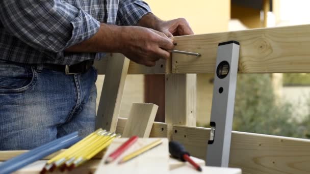 スクリュードライバー付きの大人の大工職人は、木製のフェンスのボードを固定するためにネジをねじ込みます。家事は自分でやれ映像. - 映像、動画