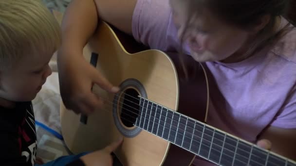 Dzieci uczą się grać na gitarze. Zbliżenie gitary i struny dłońmi dzieci. - Materiał filmowy, wideo
