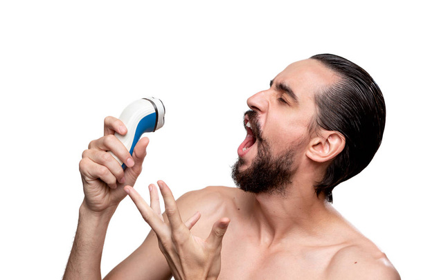 Šťastný vousatý muž s knírkem používá elektrický holicí strojek jako mikrofon, který se nachází v izolovaném prostředí na bílém pozadí. Užíváte si ranní rutinní a holicí.  - Fotografie, Obrázek