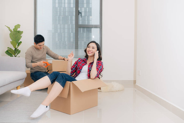 Joyeux jeune couple déménageant dans leur nouvel appartement, s'amusant et chevauchant dans des boîtes en carton à la nouvelle maison
 - Photo, image