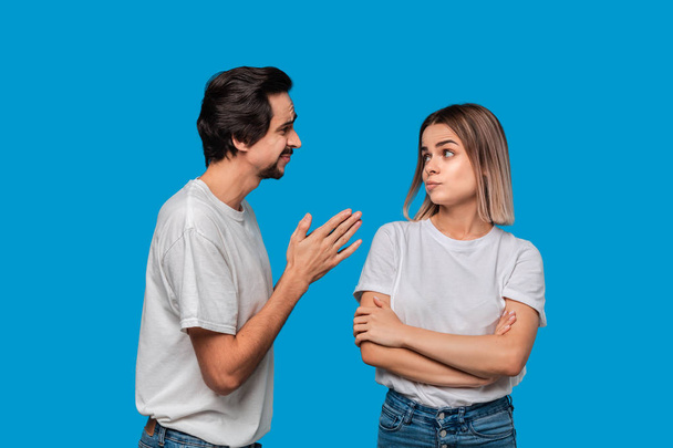 Brunet bearded man with mustaches in white t-shirt and blue jeans asking his girlfriend for forgiveness isolated over blue background. Concept of guilt. - Photo, Image