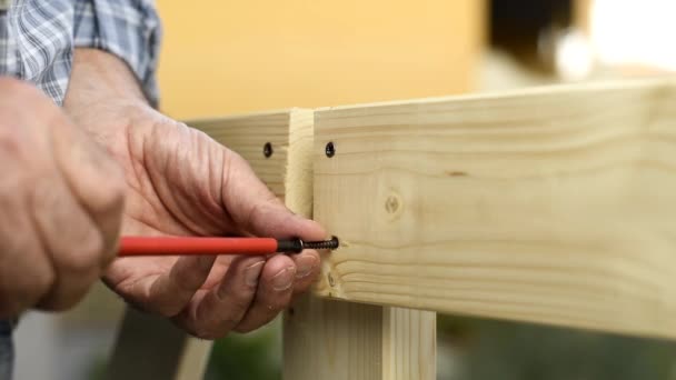 Adult carpenter craftsman with screwdriver screw the screw to fix the boards of a wooden fence. Housework do it yourself. Footage. - Footage, Video