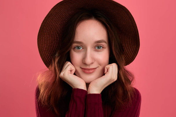 Close-up portrait of a happy beautiful brunette girl in a wide-brimmed hat posing on a dark pink background. - Zdjęcie, obraz