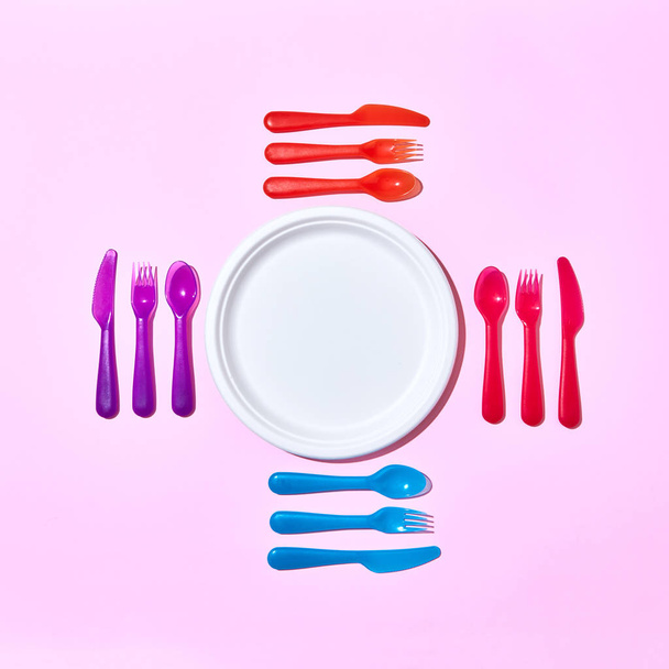 Eating set from disposable plastic cutlery, serving around paper white plate on a pastel pink background with copy space. Flat lay. - 写真・画像
