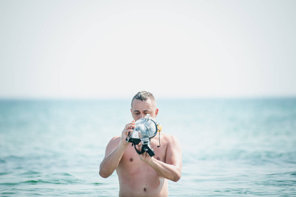 Homem com máscara de natação na mão vai para a água
 - Foto, Imagem