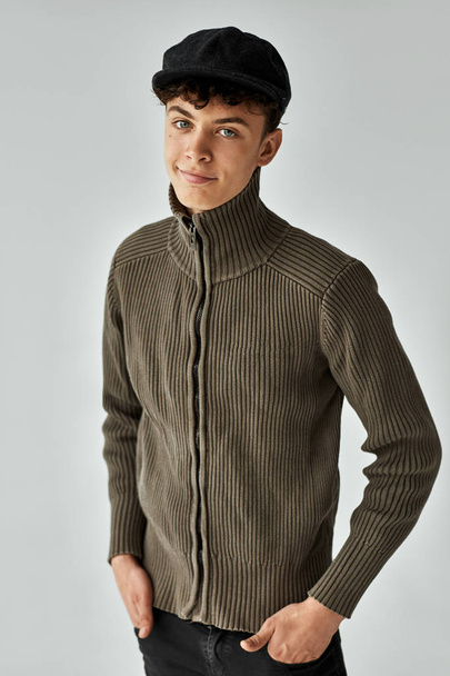 Portrait of handsome teen in knitted sweater and black cap posing in studio - Foto, Bild