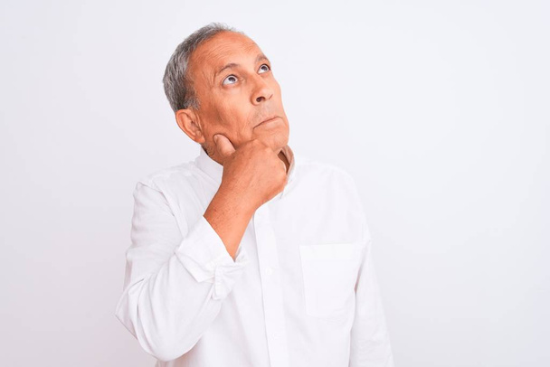 Senior grey-haired man wearing elegant shirt standing over isolated white background with hand on chin thinking about question, pensive expression. Smiling with thoughtful face. Doubt concept. - Photo, Image